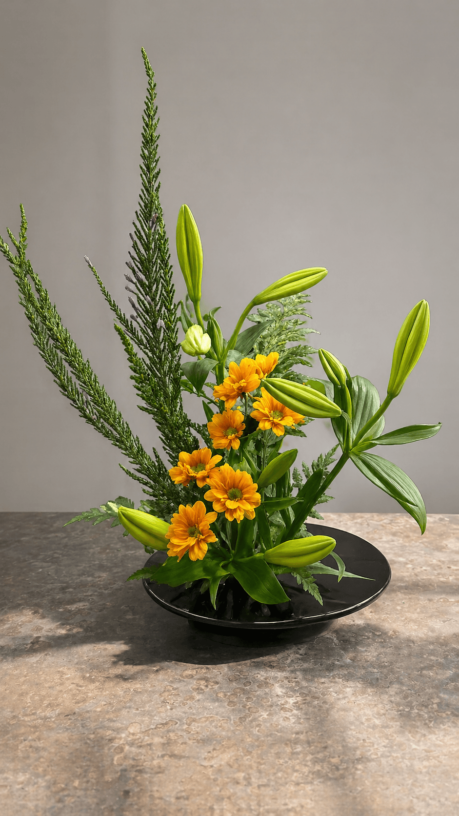 Ikebana arrangement of orange lilies and marigolds in a black dish